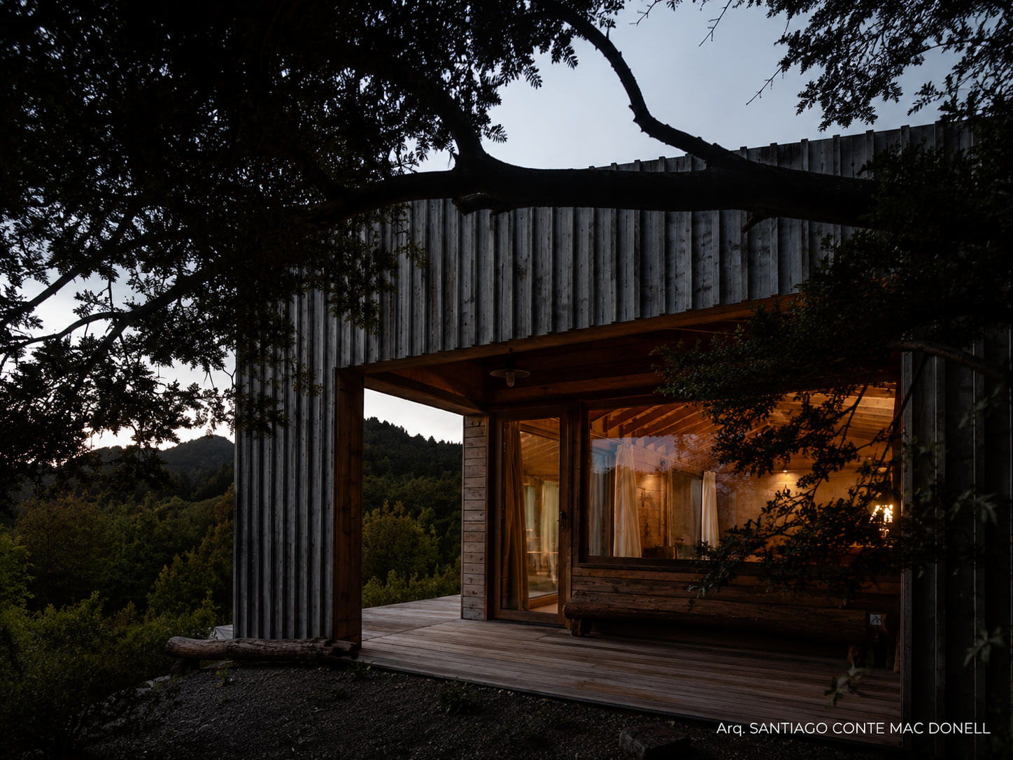 Cabaña al atardecer con ventanal de PVC iluminado y deck en el bosque